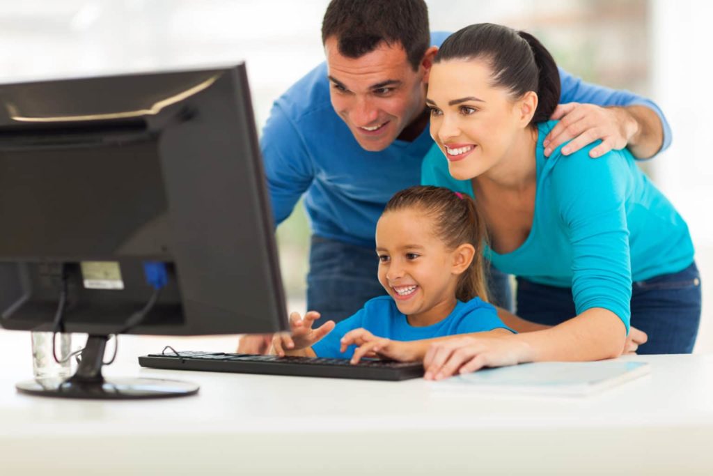 Happy child studying maths and English at the computer with her parents